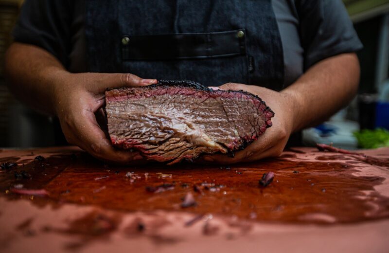 Hands holding a cooked brisket over a wooden board