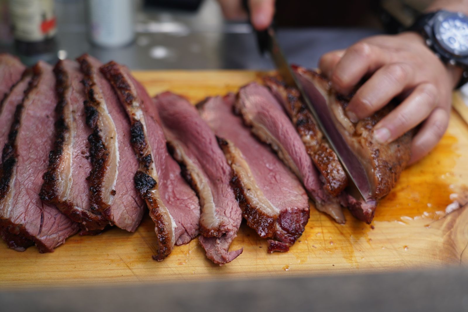 A cutter slicing smoked brisket with a dark bark and a pink smoke ring on a wooden board
