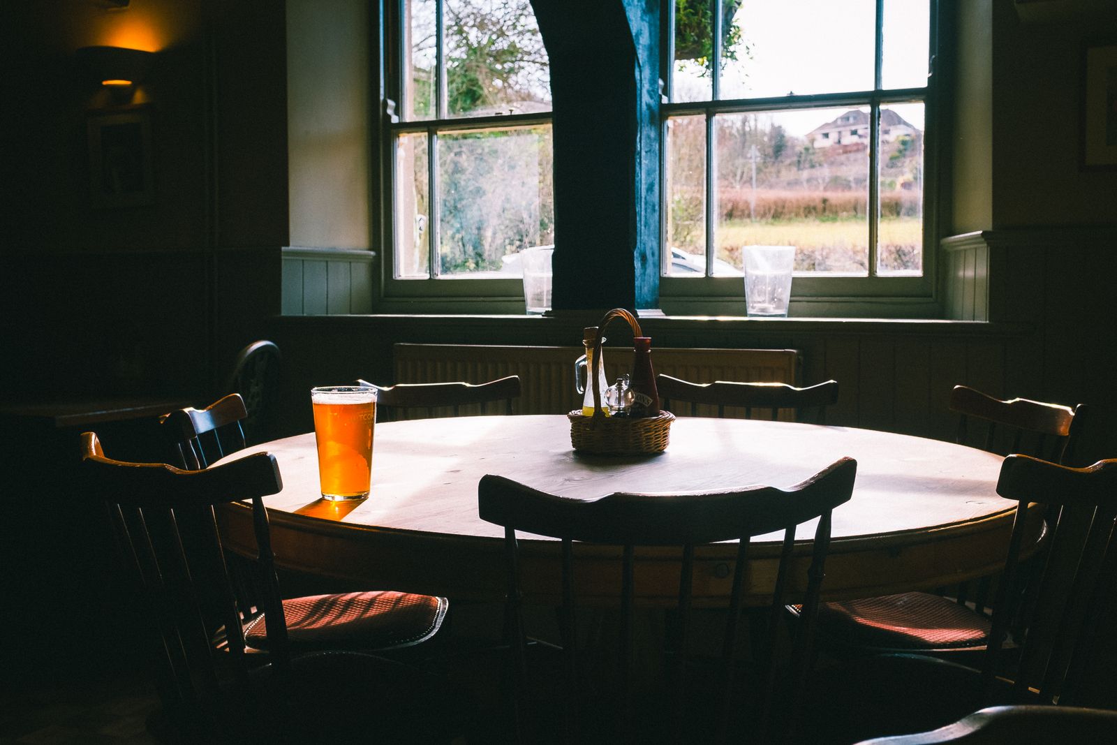 A sunlit pub dining room with a round table and a glass of beer by the window