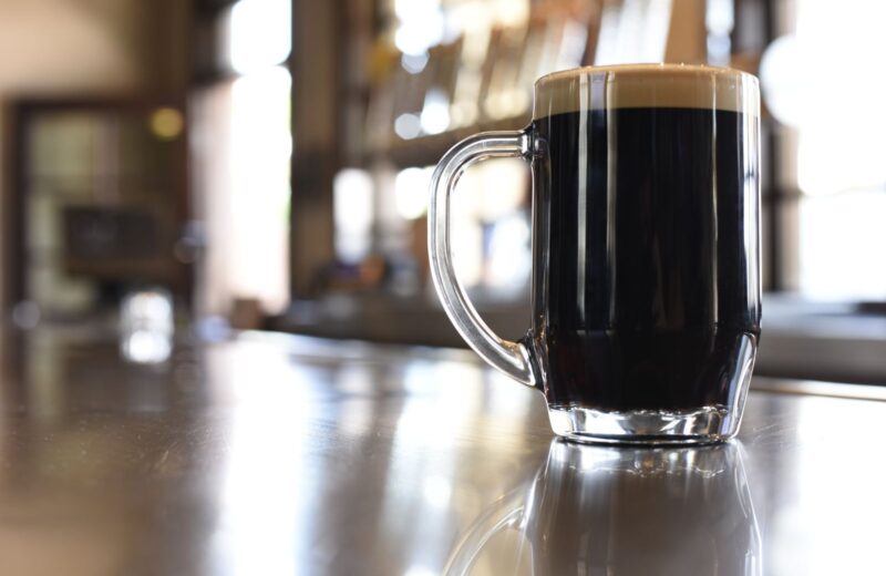A glass of dark beer with a creamy head on a bar counter