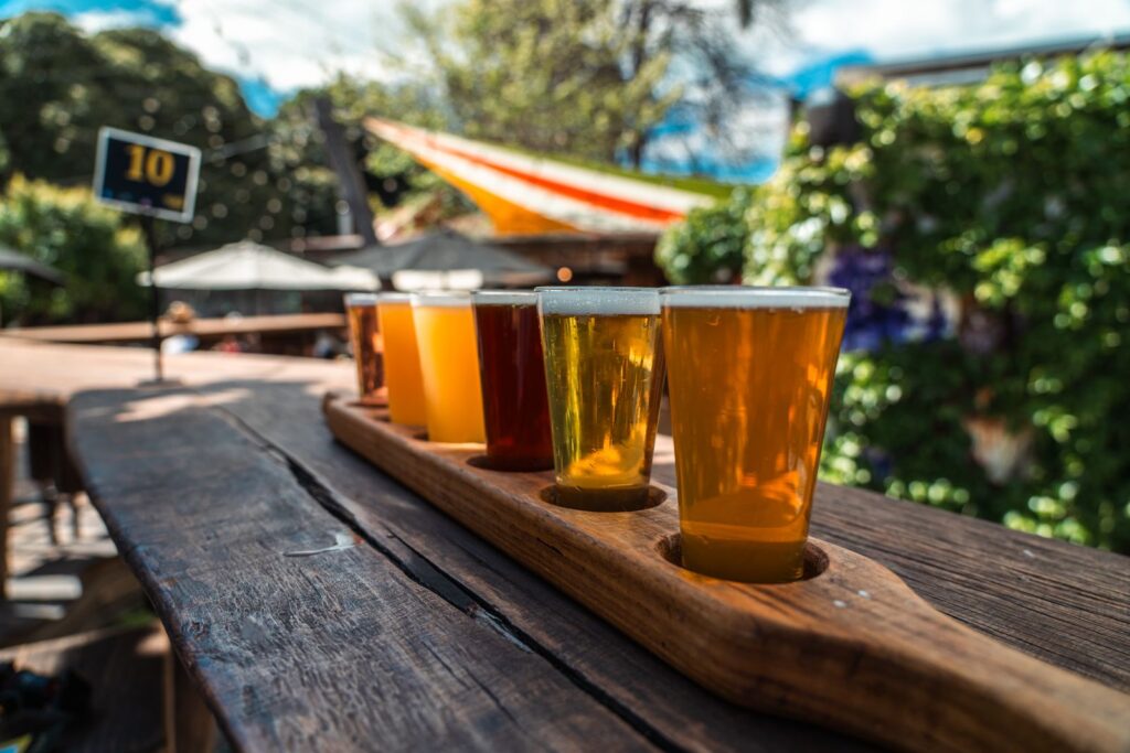 A flight of four beers from pale to dark on a wooden board outdoors