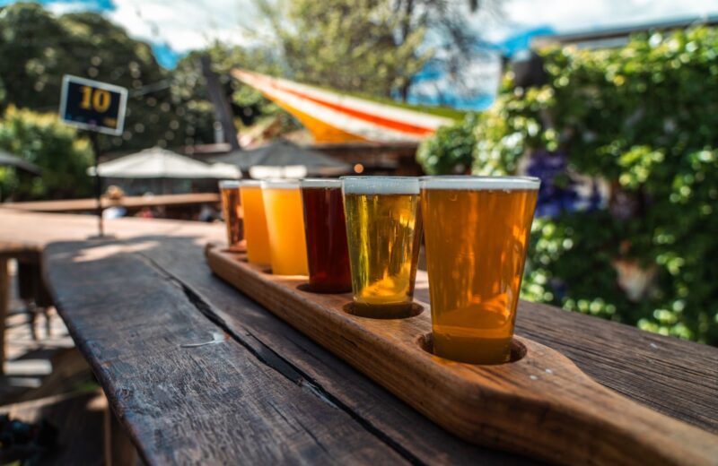 A flight of four beers from pale to dark on a wooden board outdoors
