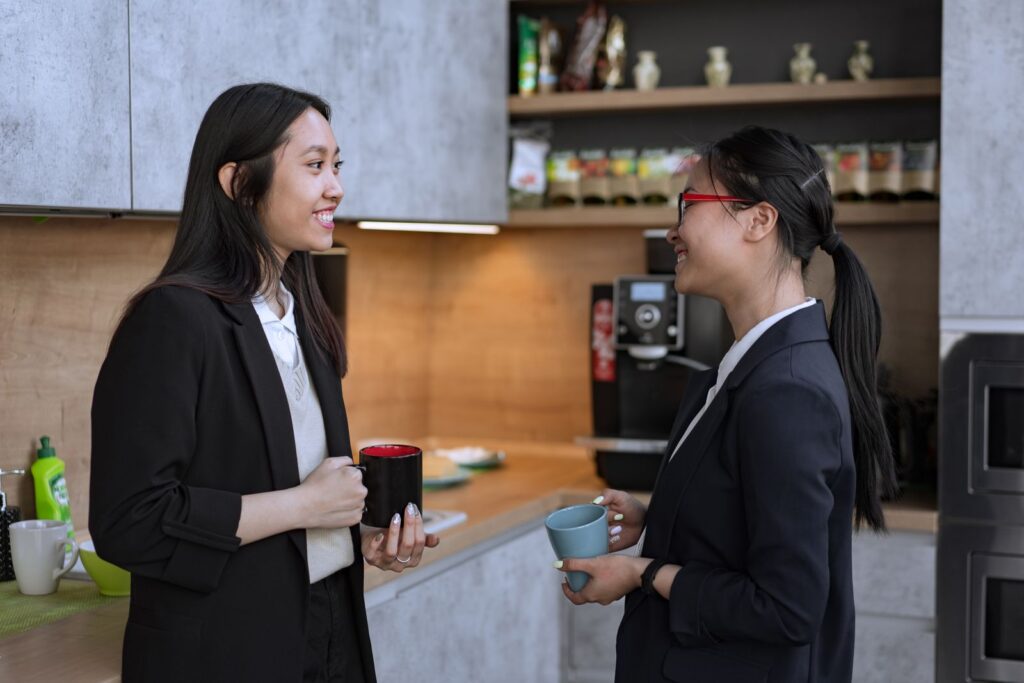 Two colleagues with mugs talking in a workplace kitchen
