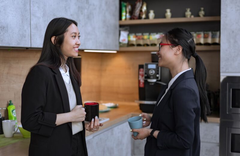 Two colleagues with mugs talking in a workplace kitchen