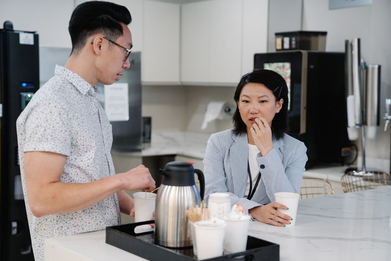 Two colleagues talking over paper cups of coffee in an office kitchen