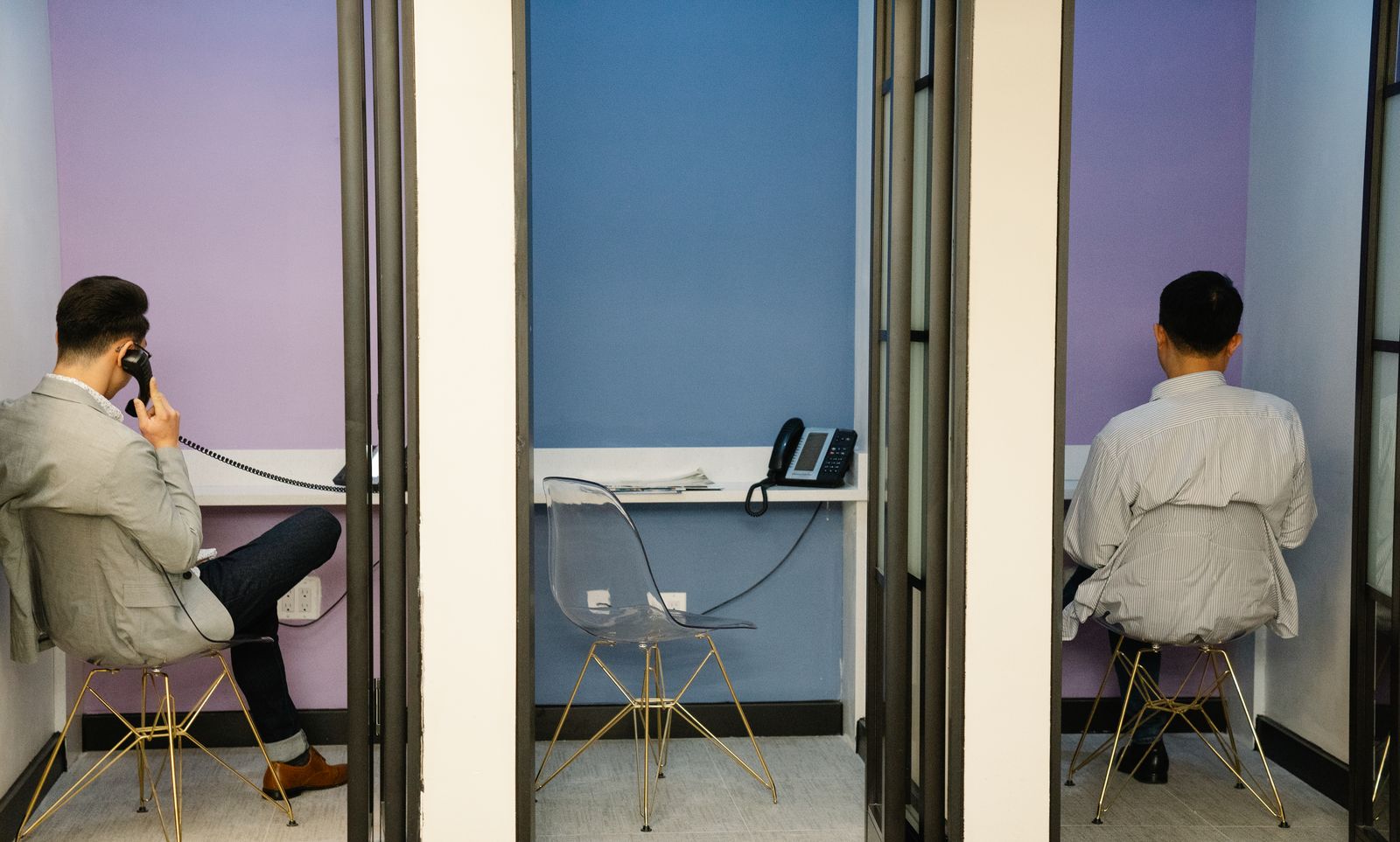People taking calls in small glass-fronted phone booths along an office wall