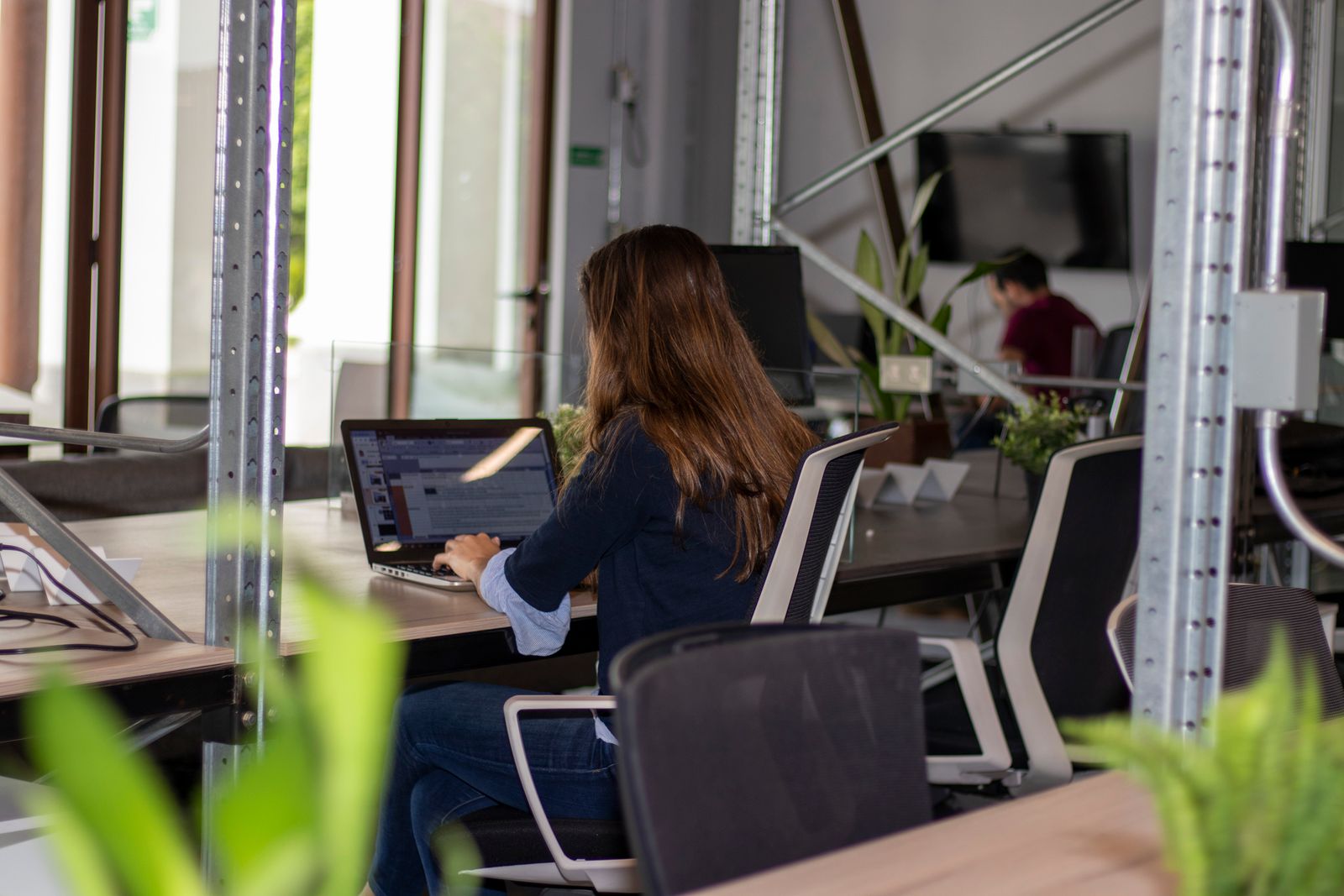 A woman working on a laptop at a desk among plants and shelves