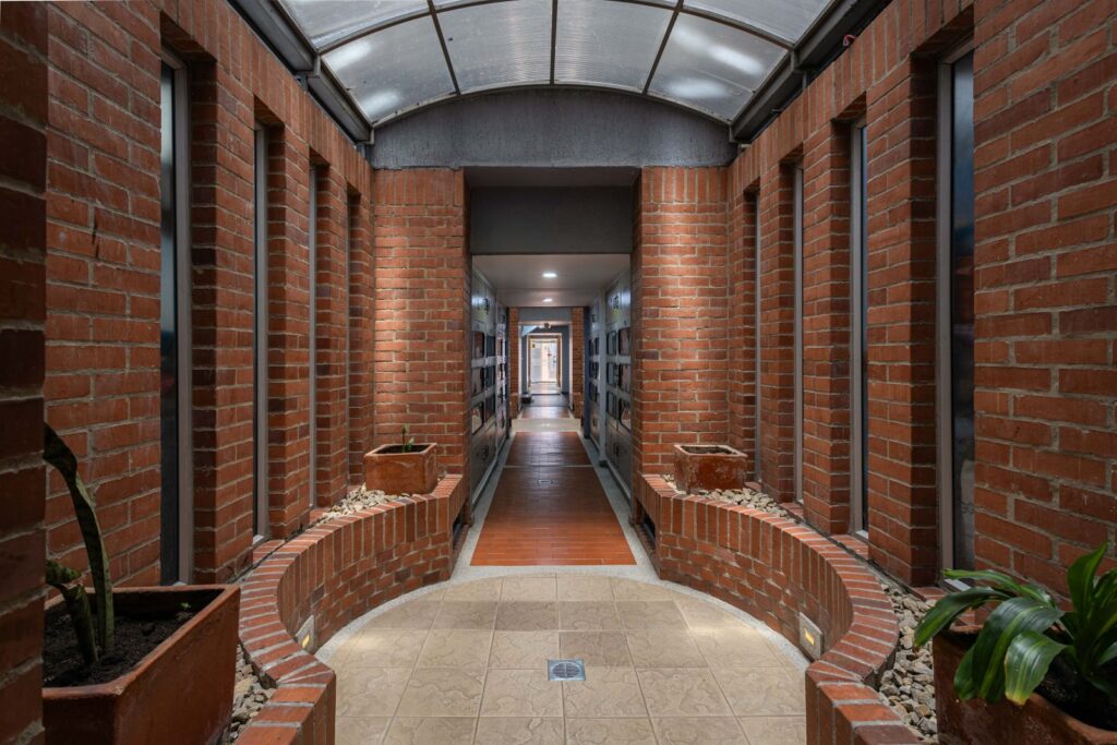 A brick corridor under a glass skylight, with plants along the walls