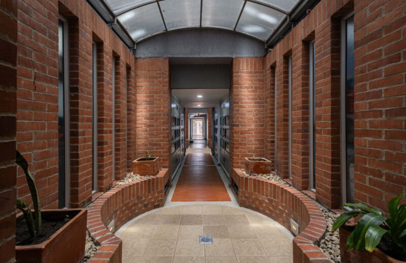 A brick corridor under a glass skylight, with plants along the walls