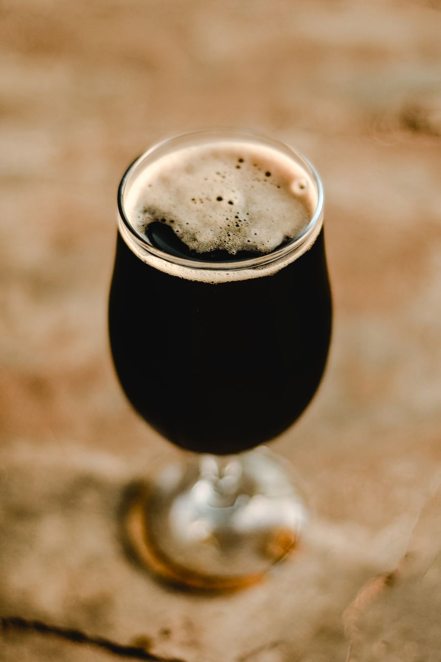 A tulip glass of dark lager with a tan head on a stone surface