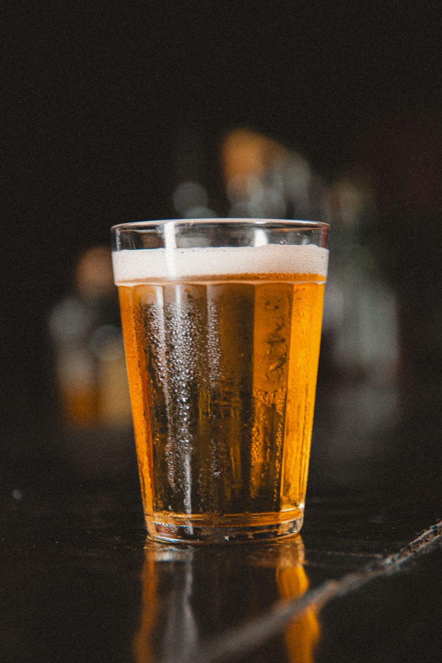A tall glass of hazy pale ale with a white head against a dark bar