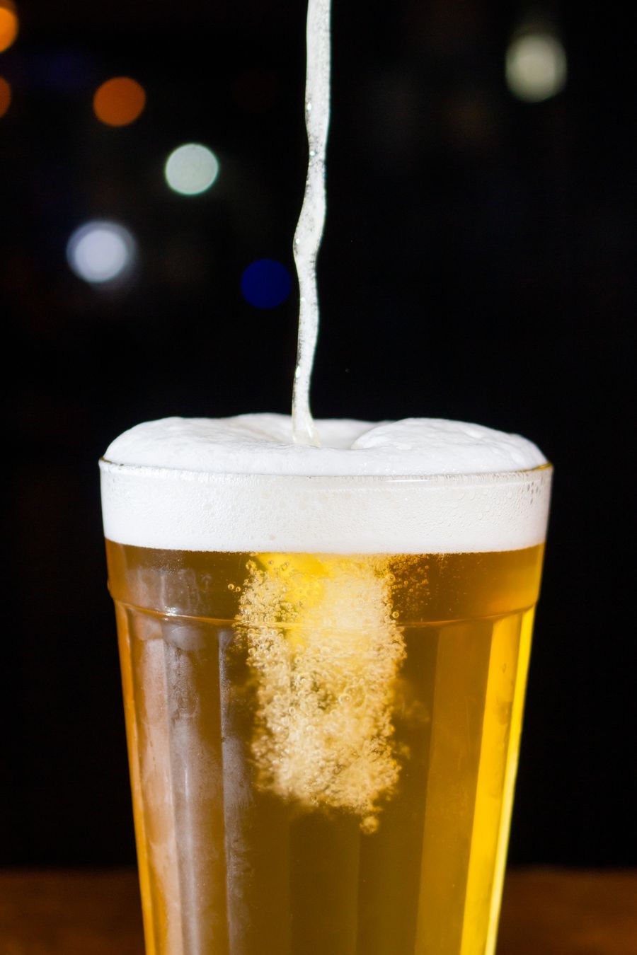 Golden pilsner being poured into a glass, foam rising, on a black background