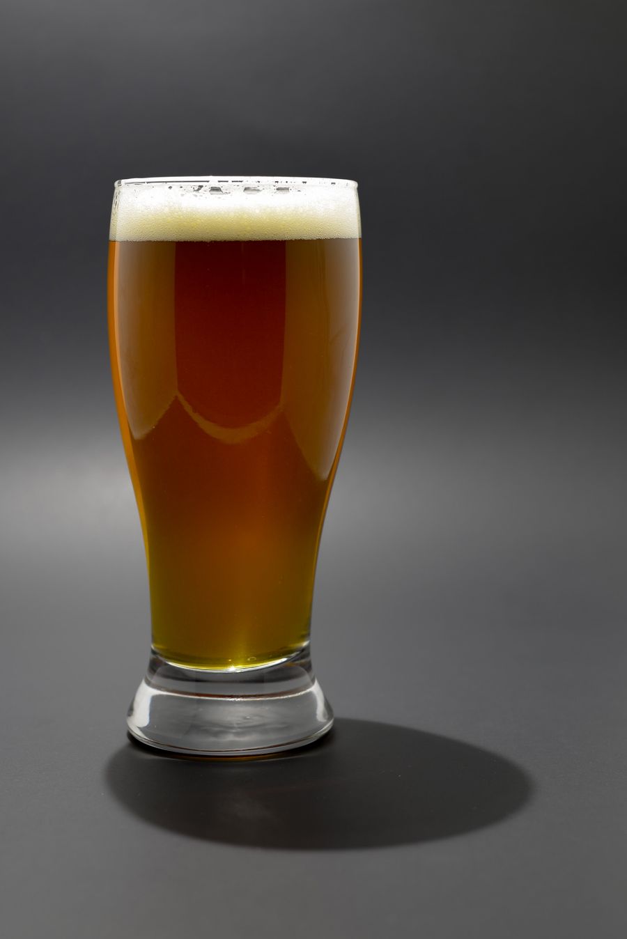 A full pint of copper-red beer with a thin head on a grey background