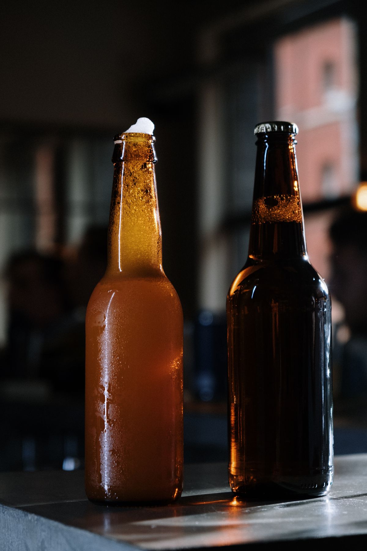 Two unlabelled beer bottles, one amber and one brown, on a bar in low light