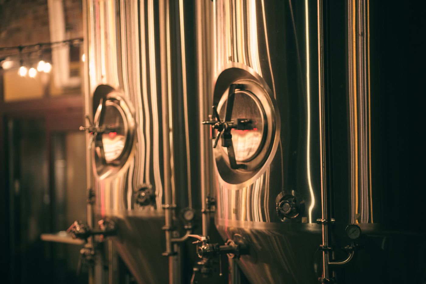 Polished steel brewing tanks with round hatches, lit warm in the brewhouse