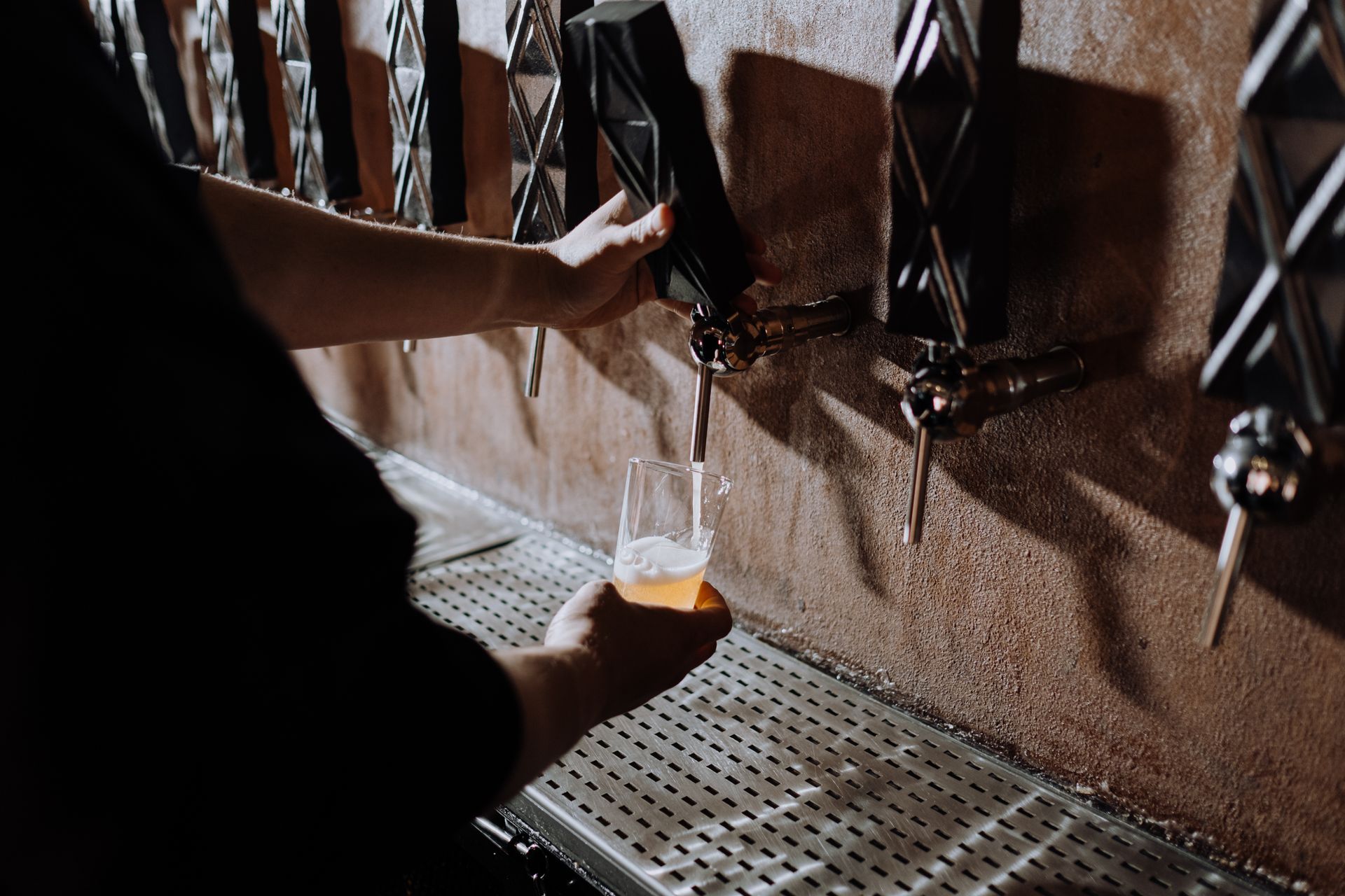 A bartender pulling a pour from a row of black tap handles against a dark plaster wall