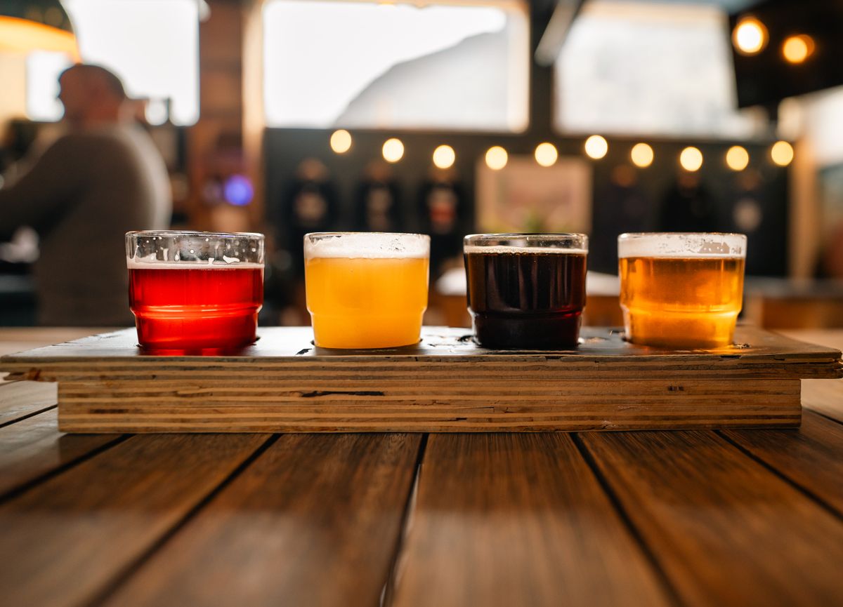 A tasting flight of four beers, pale to dark, on a wooden paddle in a taproom