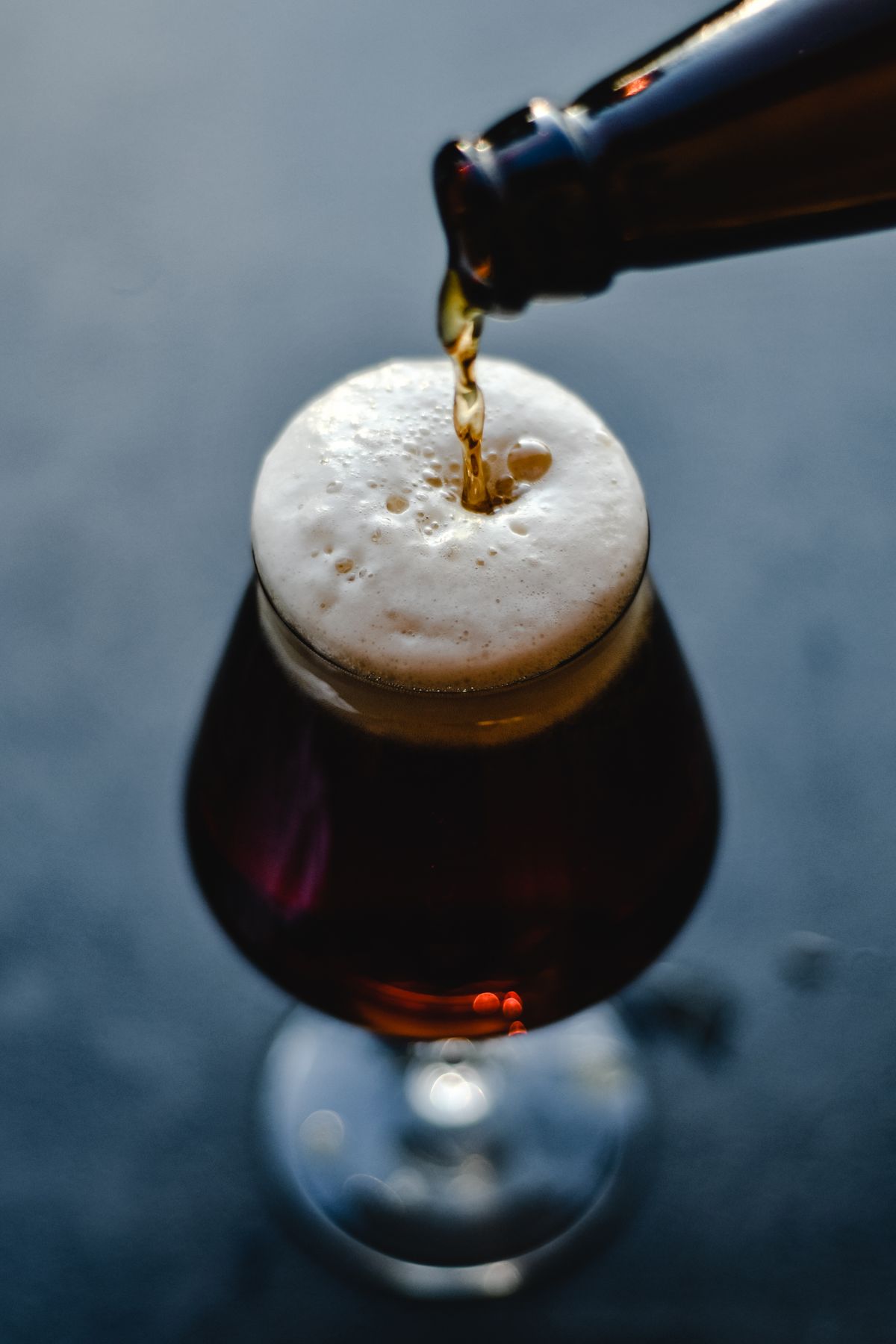 Dark beer being poured into a glass, the foam rising in low light