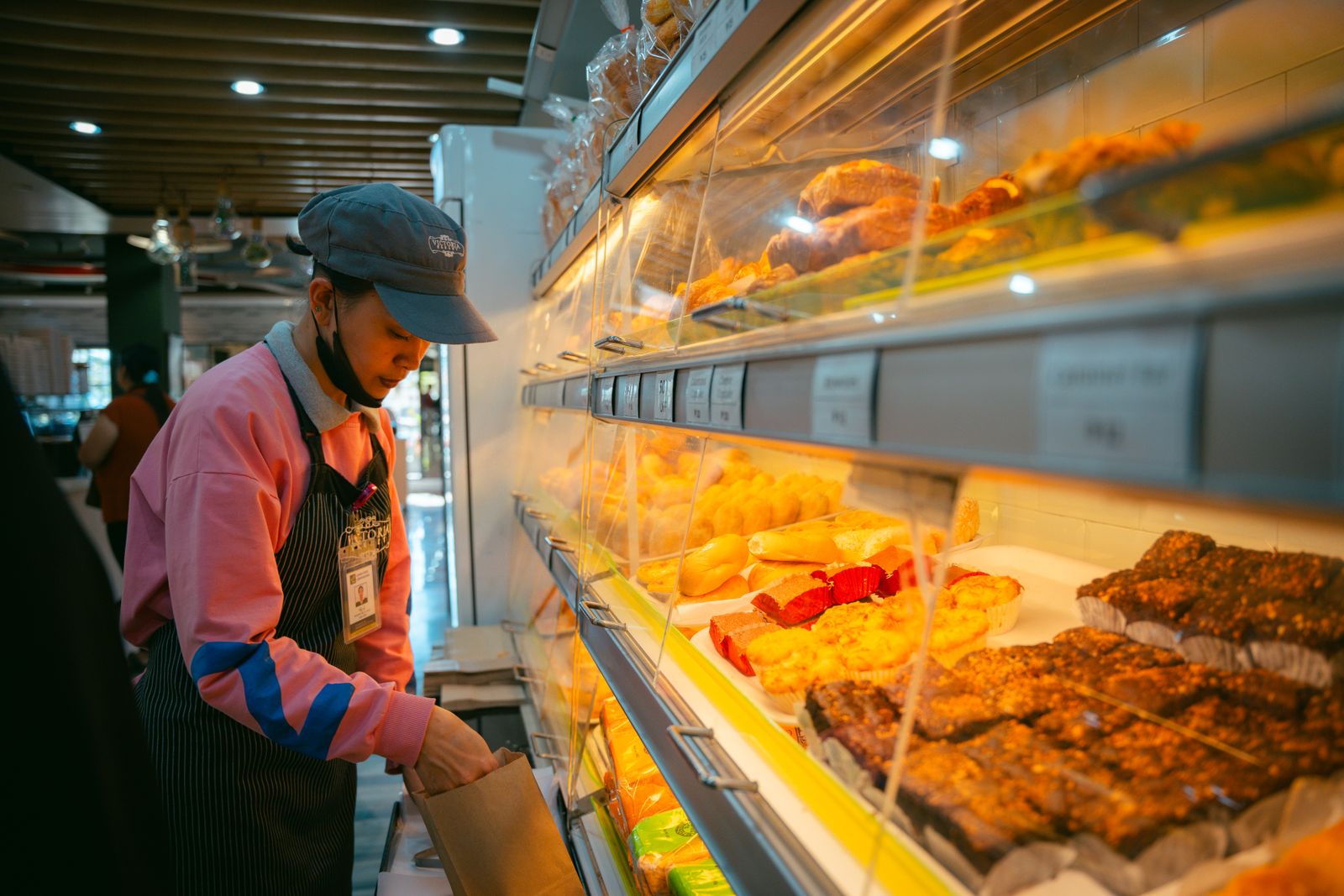 A bakery worker in an apron arranging pastries in a lit display case