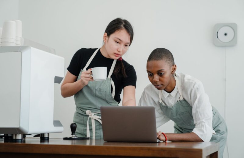 A cafe owner showing a new colleague the ordering system on a laptop