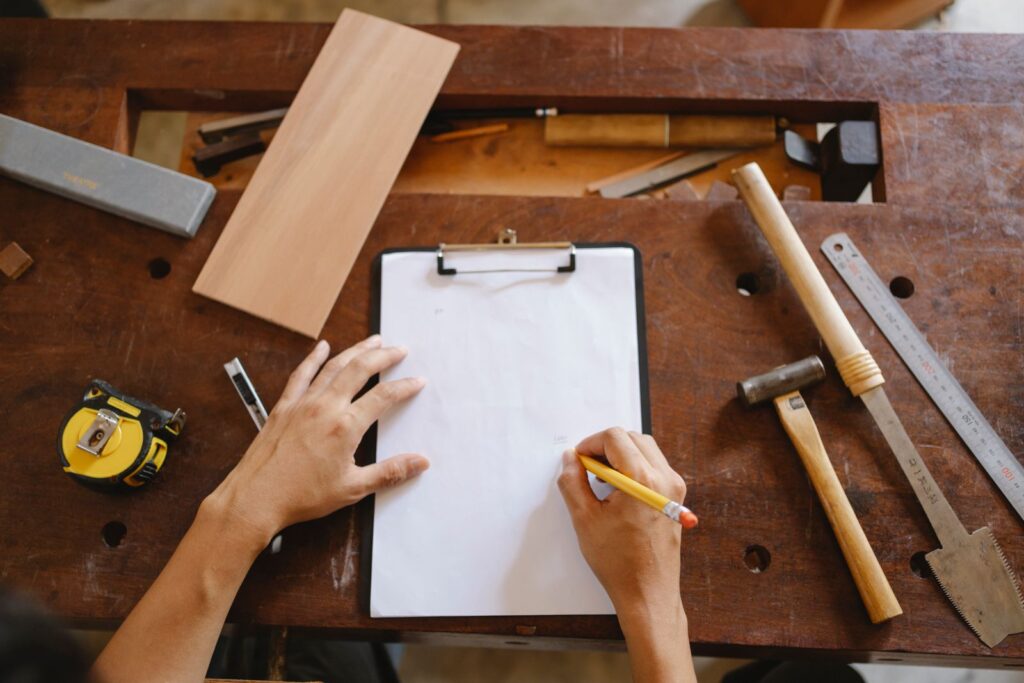A tradesperson writing figures on a clipboard on a workbench beside tools