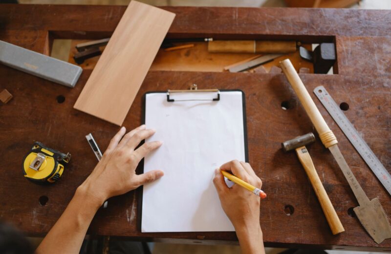 A tradesperson writing figures on a clipboard on a workbench beside tools