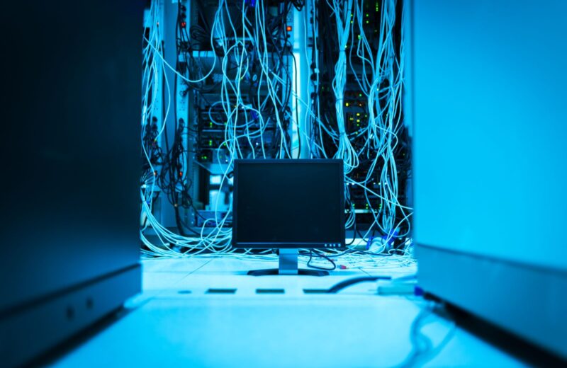 Bundles of network cables hanging behind a monitor in a blue-lit server room