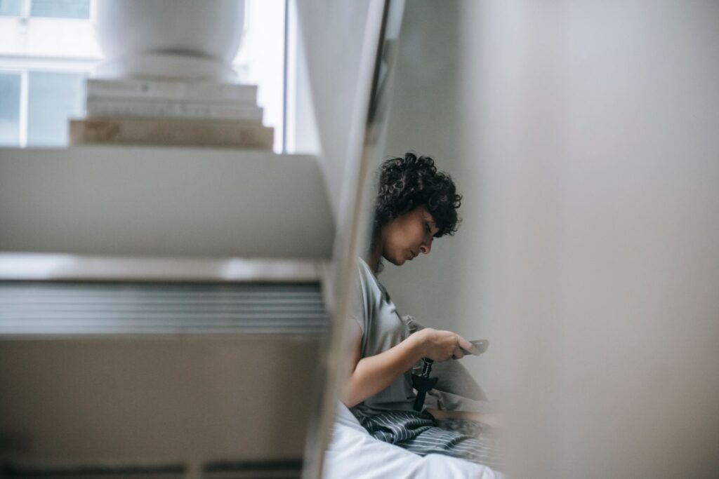A person typing a message on a phone beside a pile of books, seen from the side