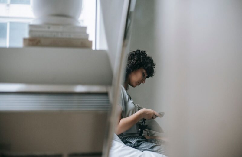 A person typing a message on a phone beside a pile of books, seen from the side