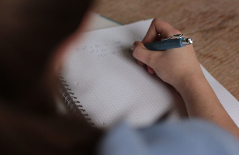 A student writing notes with a pen in a spiral notebook