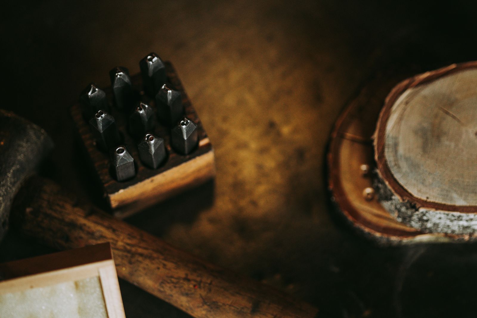 A set of steel letter punches in a holder on a dark wooden workbench