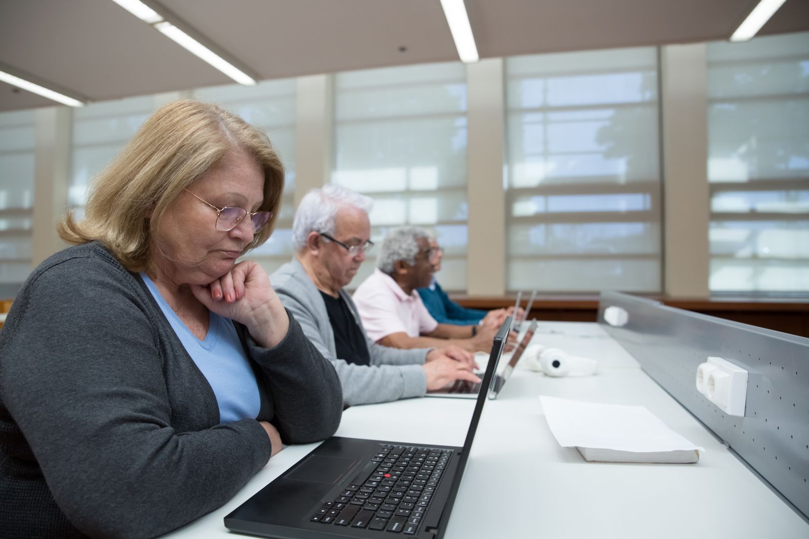 Older adults working on laptops side by side at a long classroom desk
