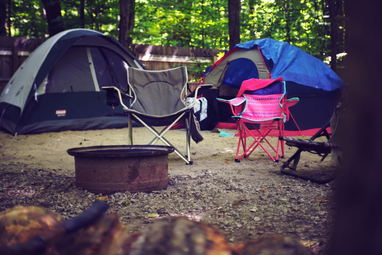 A campsite in the woods with dome tents, folding chairs and a round fire pit