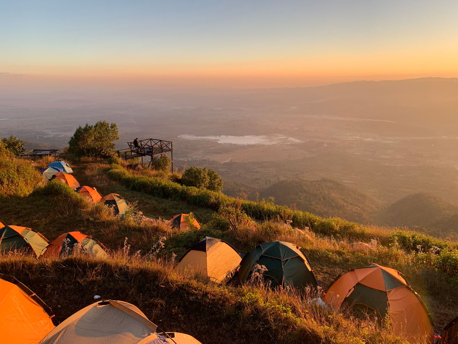 Tents pitched on a grassy hillside above a misty valley at sunrise