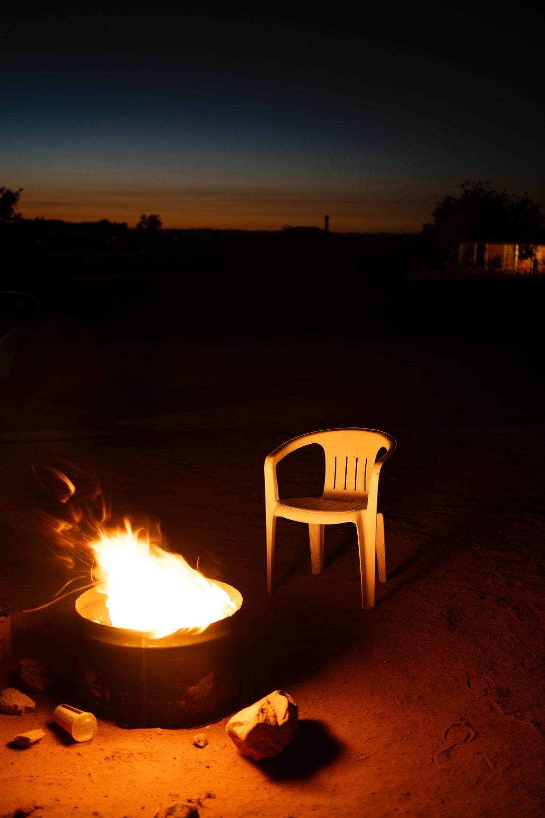 An empty folding chair beside a campfire at dusk