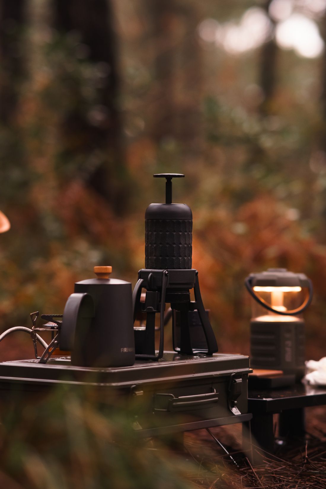 A camp percolator, a kettle and a small lantern on a table in an autumn forest