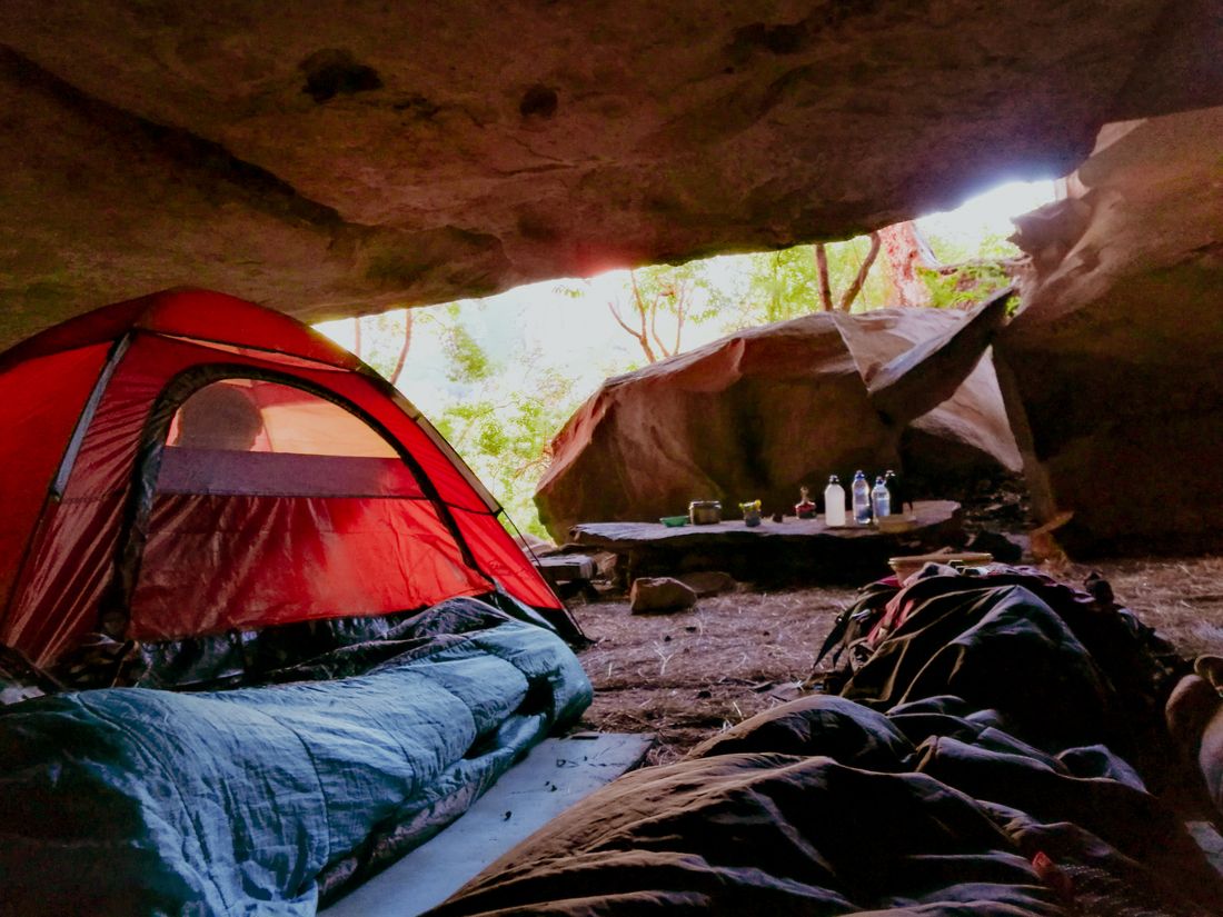 A red tent and an open sleeping bag under a rock overhang