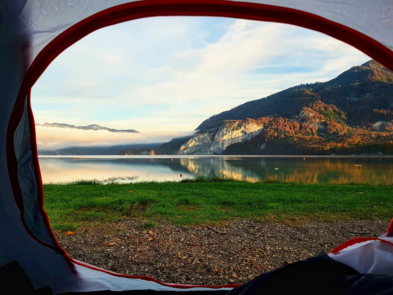 A lake, a meadow and wooded hills seen through the round door of a tent