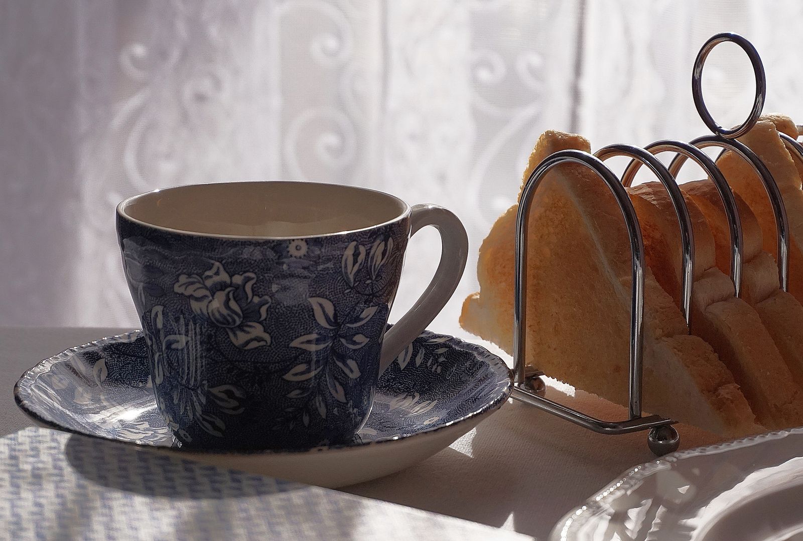 A blue patterned teacup and saucer next to a toast rack on a breakfast table