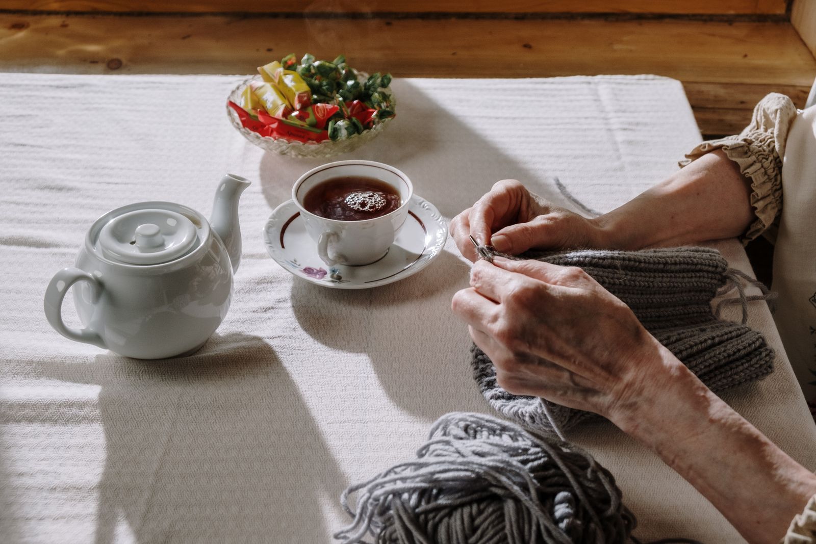 Hands knitting at a table set with a teapot, a cup of tea and a bowl of fruit