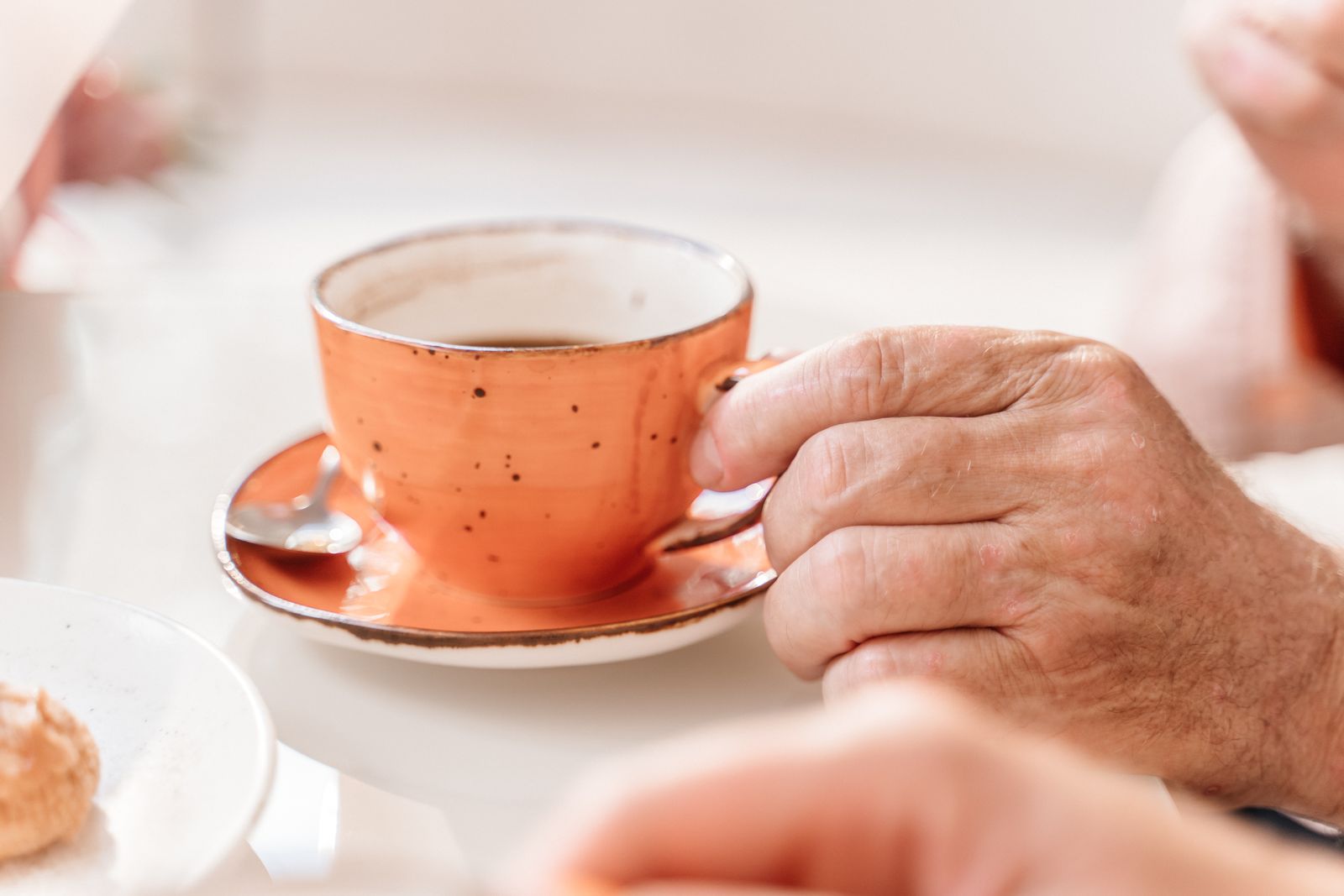 An older person's hand holding an orange cup on a wooden table