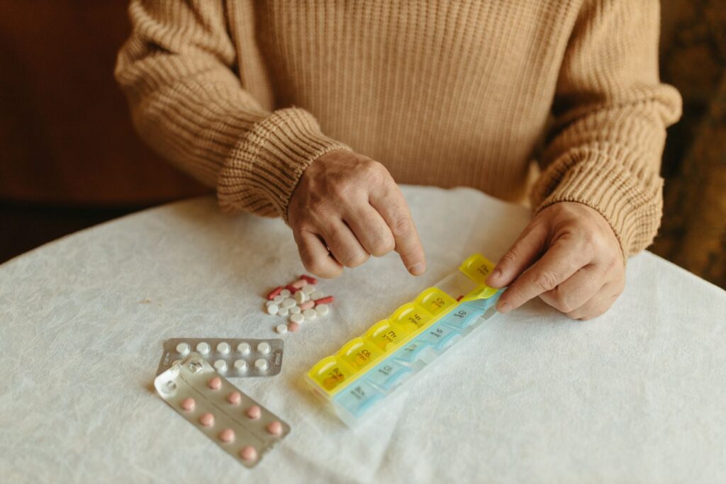 Hands sorting tablets into a weekly pill organiser on a table