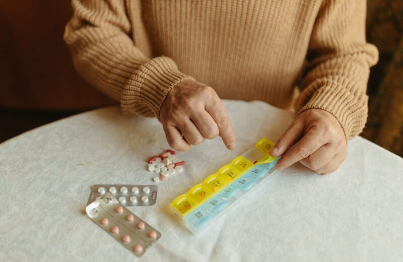 Hands sorting tablets into a weekly pill organiser on a table