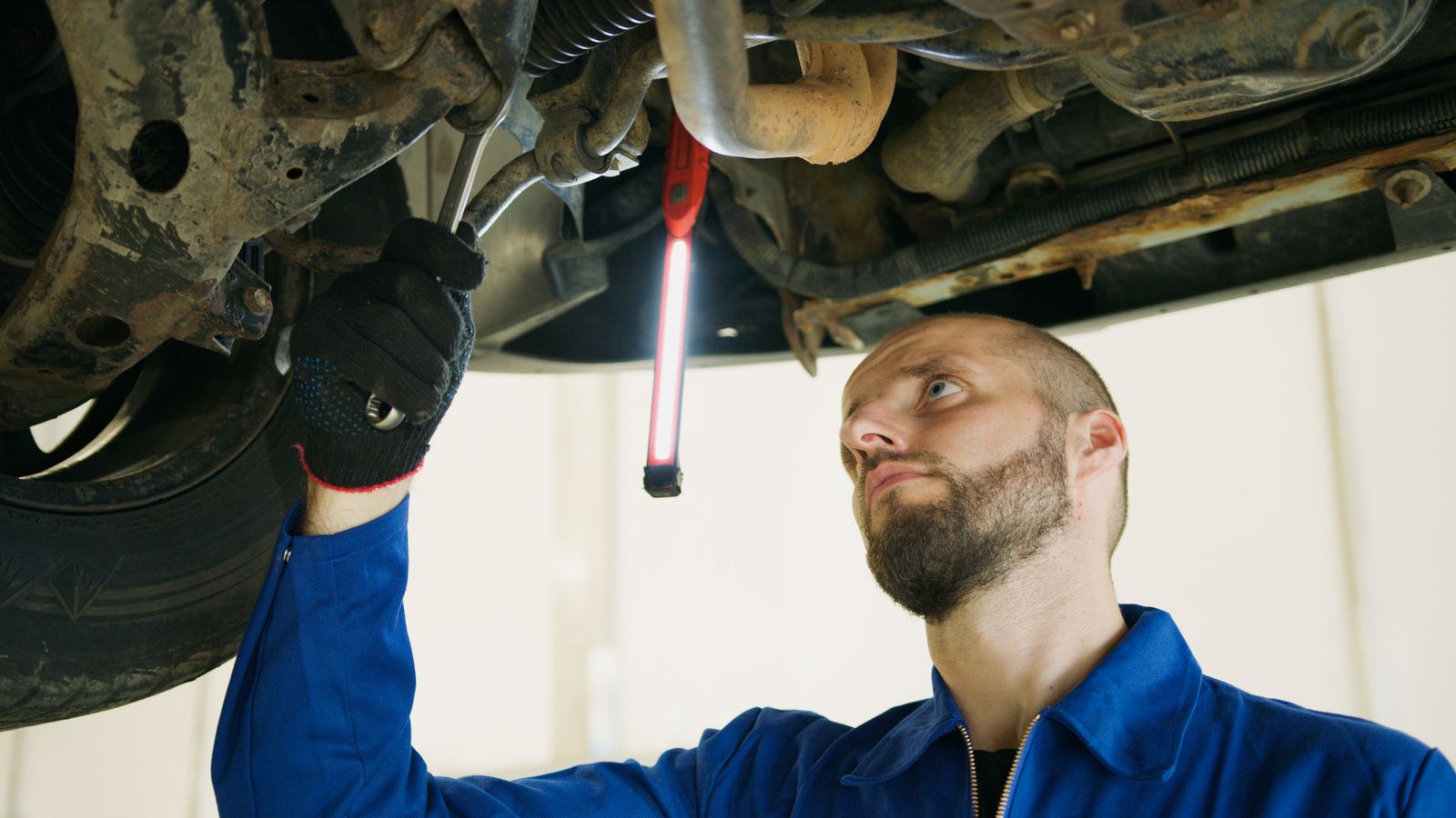 A technician with a work light checking the underside of a car