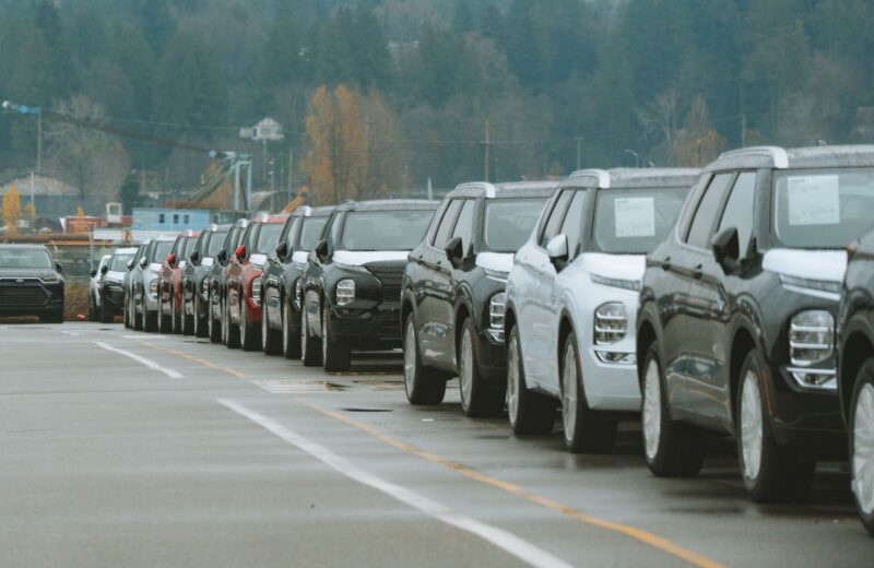 A row of SUVs parked on a dealer lot on a grey day, paper sheets on their windshields