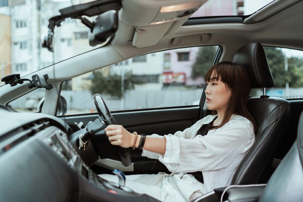 A woman driving a car through town, seen from the passenger seat