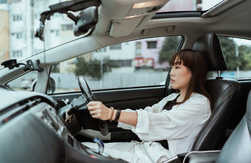 A woman driving a car through town, seen from the passenger seat