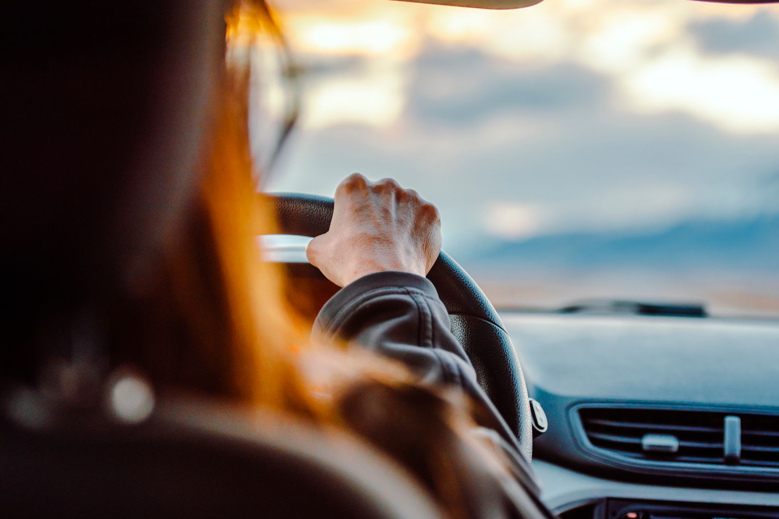 A driver's hand on the steering wheel on a test drive, low sun through the windshield