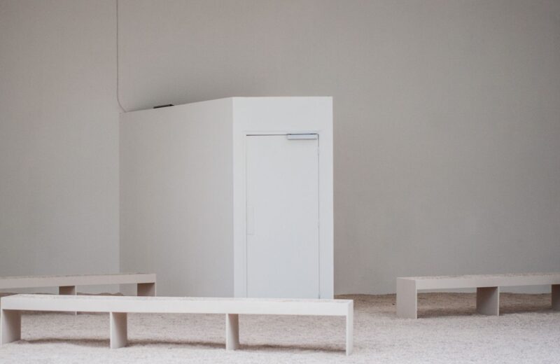 Empty white gallery room with low benches and a plinth
