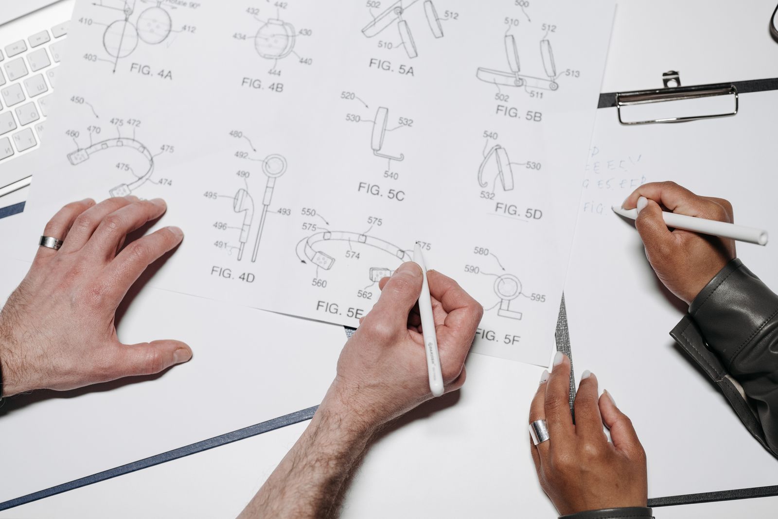 Two pairs of hands over technical line drawings on white paper